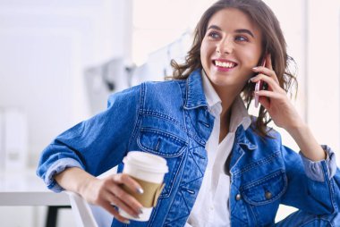 Kafede kahve içip cep telefonuyla konuşan genç bir kadın.