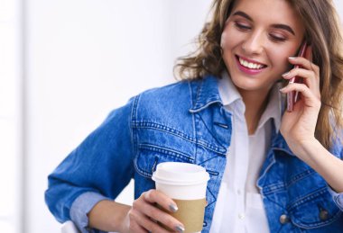 Kafede kahve içip cep telefonuyla konuşan genç bir kadın.