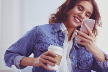 Kafede kahve içip cep telefonuyla konuşan genç bir kadın.