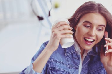 Kafede kahve içip cep telefonuyla konuşan genç bir kadın.