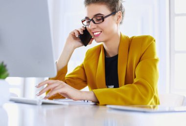 İş kadını ofiste bilgisayar ve cep telefonu kullanarak işine konsantre oluyor.