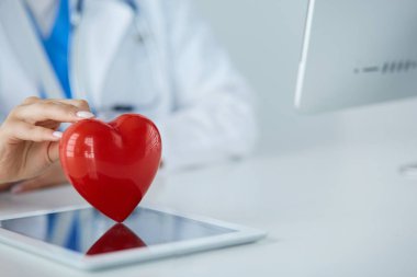 Steteskop tutan, kalbi hafif arka planda olan kadın bir doktor.