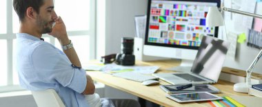İnternette çalışırken bilgisayarın ve dizüstü bilgisayarın önünde grafik stüdyosunda oturan genç tasarımcının portresi.
