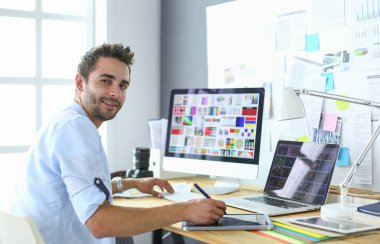 İnternette çalışırken bilgisayarın ve dizüstü bilgisayarın önünde grafik stüdyosunda oturan genç tasarımcının portresi.