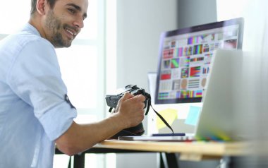 İnternette çalışırken bilgisayarın ve dizüstü bilgisayarın önünde grafik stüdyosunda oturan genç tasarımcının portresi.