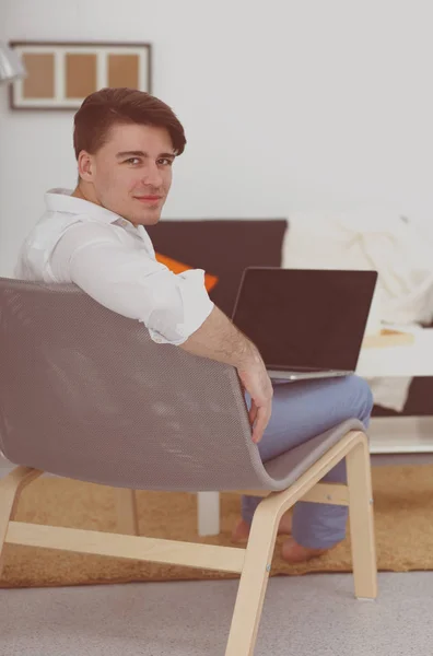Genç adam sandalyede oturuyor ve dizüstü bilgisayarla çalışıyor. — Stok fotoğraf