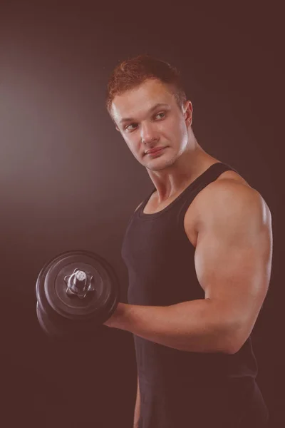 Cara muscular fazendo exercícios com halteres sobre fundo escuro — Fotografia de Stock