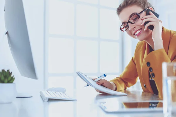 Portrait of beautiful woman making call while sitting at her workplace in front of laptop and working on new project — Stock Photo, Image