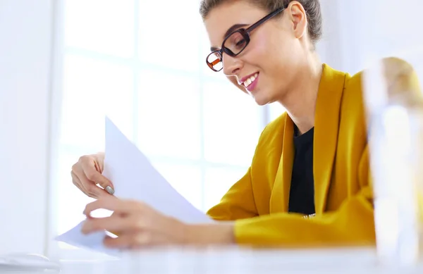 Schöne junge Geschäftsfrau erledigt ein paar Papierkram, während sie am Schreibtisch vor dem Laptop sitzt — Stockfoto