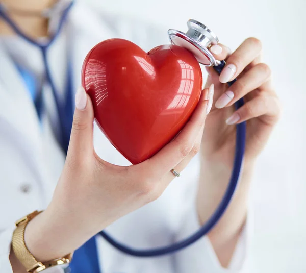 A doctor with stethoscope examining red heart, isolated on white background — Stock Photo, Image