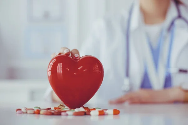 Doctor en bata blanca con estetoscopio sosteniendo píldoras y corazón de plástico aislado en blanco — Foto de Stock