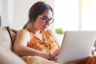 Evde dizüstü bilgisayar üzerinde çalışan kanepede oturan genç kadın