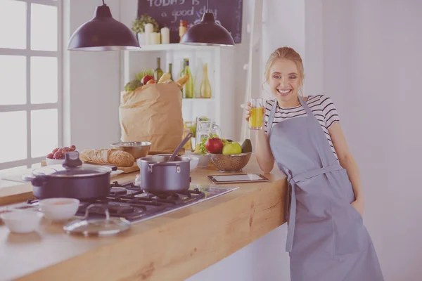 Atractiva mujer sosteniendo un vaso de jugo de naranja mientras está de pie en la cocina — Foto de Stock