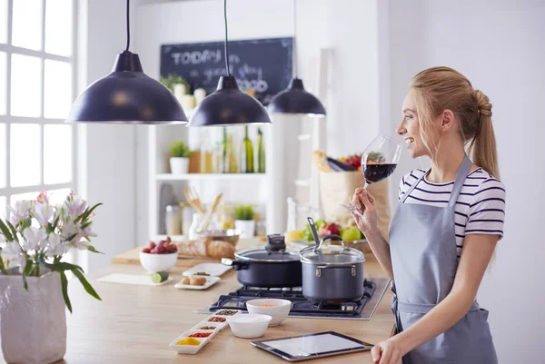 Mujer bonita bebiendo un poco de vino en casa en la cocina —  Fotos de Stock