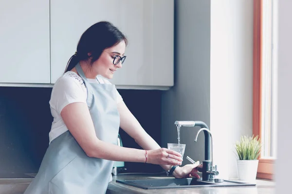 Menselijke hand holding glas gieten vers drinkwater bij keukenkraan — Stockfoto