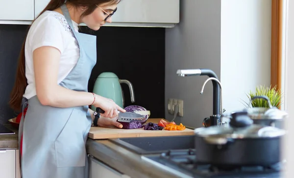 Junge Frau schneidet Gemüse in Küche neben Schreibtisch — Stockfoto