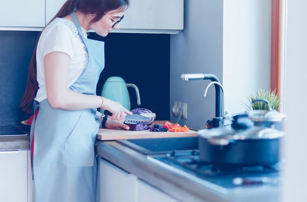 Ung kvinna skära grönsaker i köket står nära skrivbordet — Stockfoto