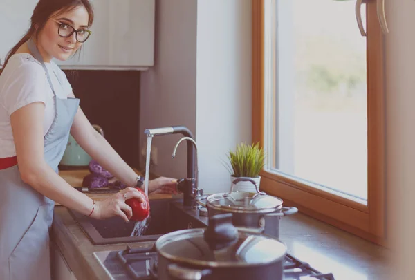 Femme lavant les légumes. Belle jeune femme lavant les légumes pour salade et souriant tout en se tenant dans la cuisine — Photo