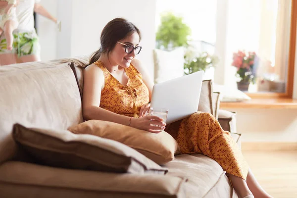 Evde dizüstü bilgisayar üzerinde çalışan kanepede oturan genç kadın — Stok fotoğraf