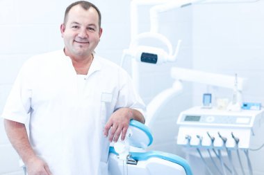 Diş kliniğinde duran gülümseyen bir dişçinin portresi.