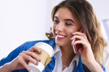 Kafede kahve içip cep telefonuyla konuşan genç bir kadın.