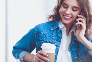 Kafede kahve içip cep telefonuyla konuşan genç bir kadın.