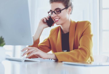 İş kadını ofiste bilgisayar ve cep telefonu kullanarak işine konsantre oluyor.