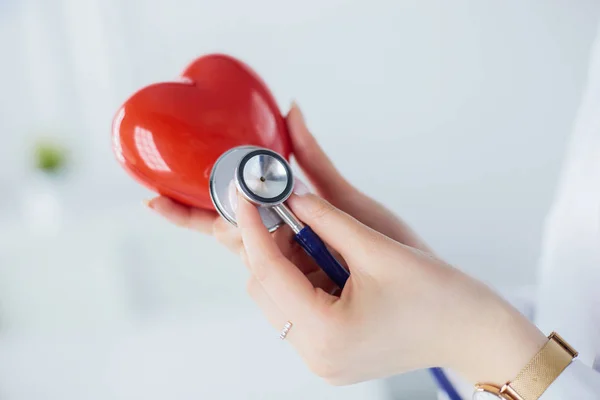 Un médecin avec stéthoscope examinant le cœur rouge, isolé sur fond blanc — Photo