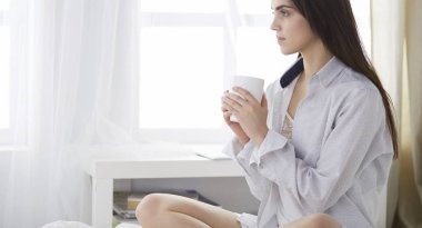 Yatakta oturup kitap okuyan ve kahvaltı yapan bir kadın.