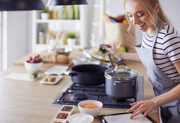 Jonge vrouw met behulp van een tablet computer om te koken in haar keuken — Stockfoto