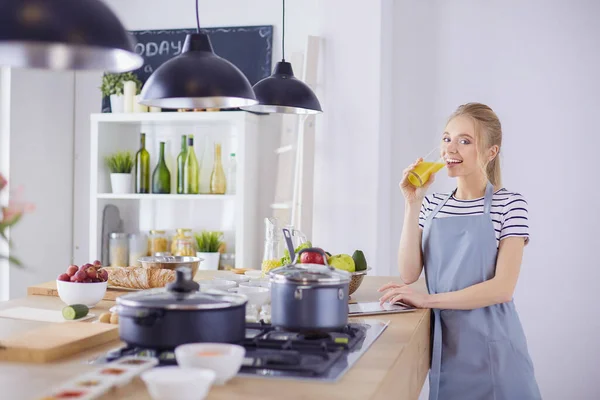 Привлекательная женщина держит стакан апельсинового сока, стоя на кухне — стоковое фото