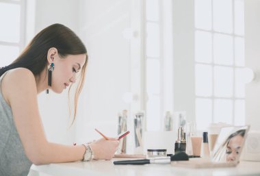 Makyaj masasında oturmuş makyajını yapan güzel bir genç kadın.