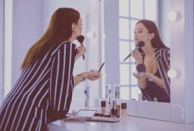 Güzel kız aynaya bakıyor ve büyük bir fırçayla kozmetik uyguluyor.