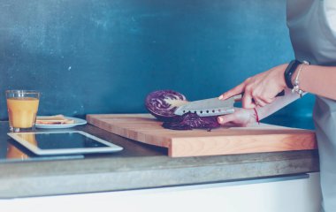 Mutfakta yemek yapmak için tablet bilgisayar kullanan genç bir kadın.