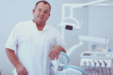 Diş kliniğinde duran gülümseyen bir dişçinin portresi.