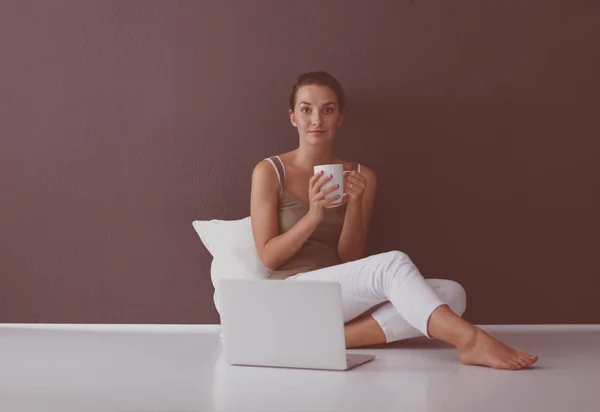 Μια όμορφη νεαρή υγιή κάθεται στο πάτωμα με ένα φλιτζάνι τσάι ή καφέ χαμογελώντας. απομονωμένο σε λευκό φόντο — Φωτογραφία Αρχείου