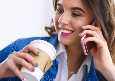 Kafede kahve içip cep telefonuyla konuşan genç bir kadın.