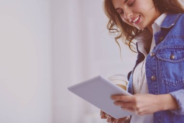 Gülümseyen kadın kahve içiyor ve kafede tablet kullanıyor.