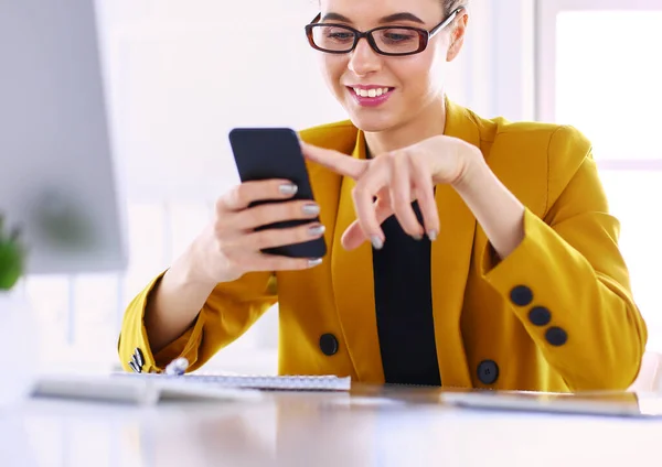 Retrato de la mujer de negocios usando el teléfono móvil y mensajes de texto mientras está sentada en el escritorio delante de la computadora portátil — Foto de Stock
