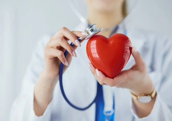 Steteskoplu bir doktor, beyaz arka planda kırmızı kalbi inceliyor. — Stok fotoğraf
