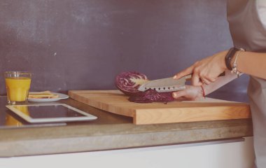 Mutfakta yemek yapmak için tablet bilgisayar kullanan genç bir kadın.