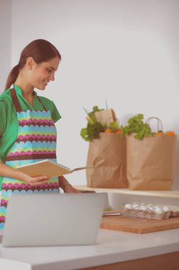 Güzel bir kadın mutfakta dizüstü bilgisayarıyla rahatlarken bir fincan kahvenin tadını çıkarıyor.