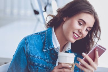 Kafede kahve içip cep telefonuyla konuşan genç bir kadın.