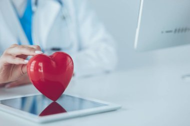 Steteskop tutan, kalbi hafif arka planda olan kadın bir doktor.