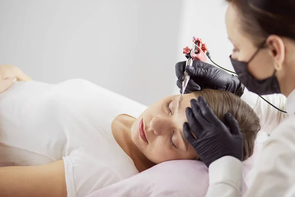 Jonge vrouw ondergaat procedure van wenkbrauw permanente make-up in schoonheidssalon — Stockfoto