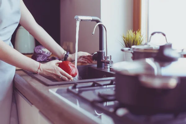 Frau wäscht Gemüse. Schöne junge Frau wäscht Gemüse für Salat und lächelt in der Küche — Stockfoto