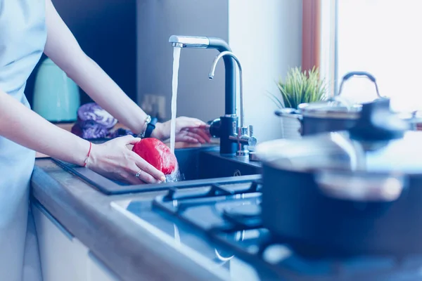 女人在洗蔬菜美丽的年轻女子一边站在厨房里一边洗蔬菜做沙拉，一边微笑 — 图库照片