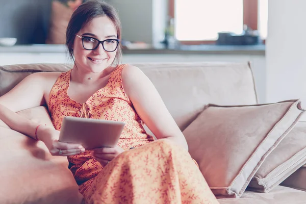 Vacker ung brunett kvinna hemma sitter på soffan eller soffa med sin Tablet PC och leende — Stockfoto