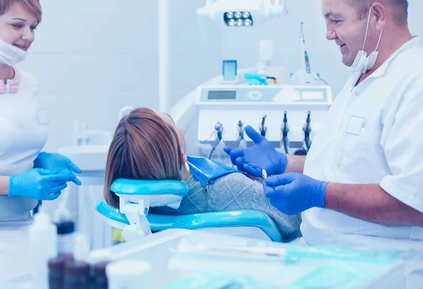 Старший чоловічий стоматолог в стоматологічному кабінеті розмовляє з пацієнткою і готується до лікування — стокове фото