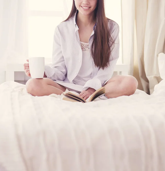 Woman sitting in bed reading a book and having breakfast — Stock Photo, Image